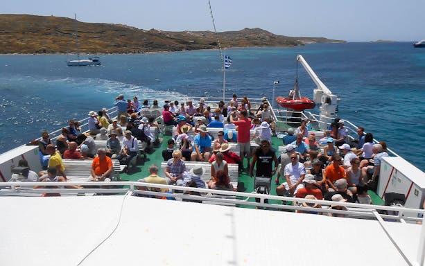 Tourists on a boat heading to Delos from Mykonos, enjoying a guided tour with skip-the-line entry.