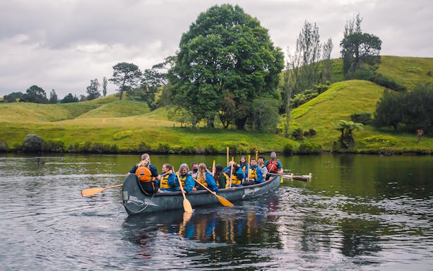 Group paddling a large canoe on a scenic river during the Big Kanu Glowworm tour from Tauranga.