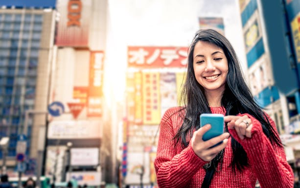 Young woman using smartphone in bustling Tokyo street, Japan, highlighting eSIM connectivity.