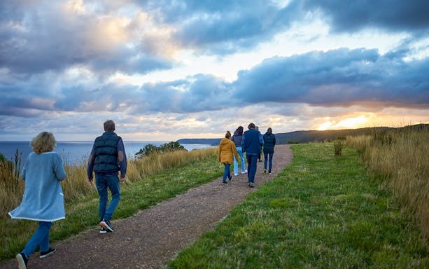 Group walking along a coastal path at sunset during the Dusk Discovery Tour.