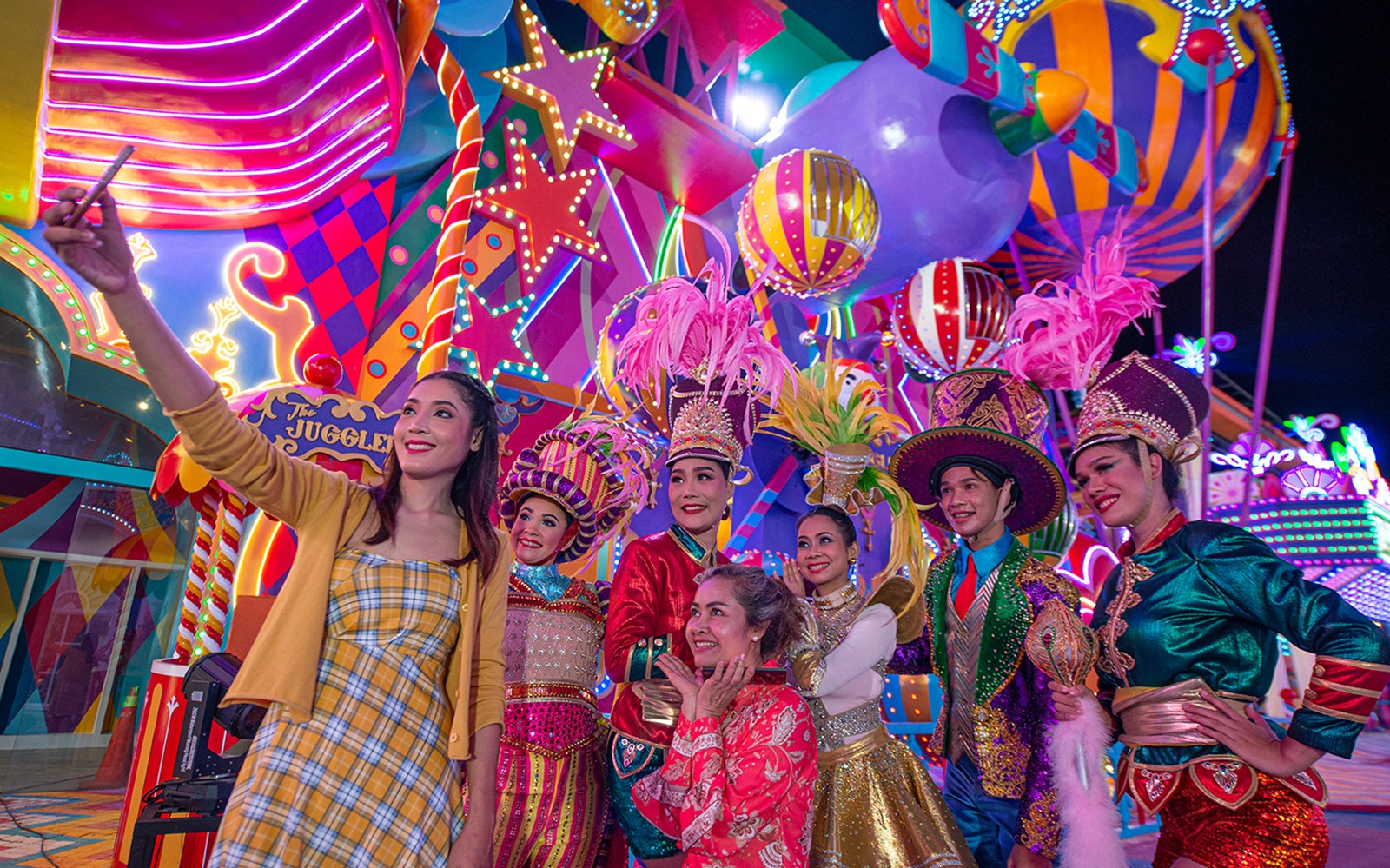 Carnival performers and visitors at Carnival Magic Park, vibrant costumes and lights.