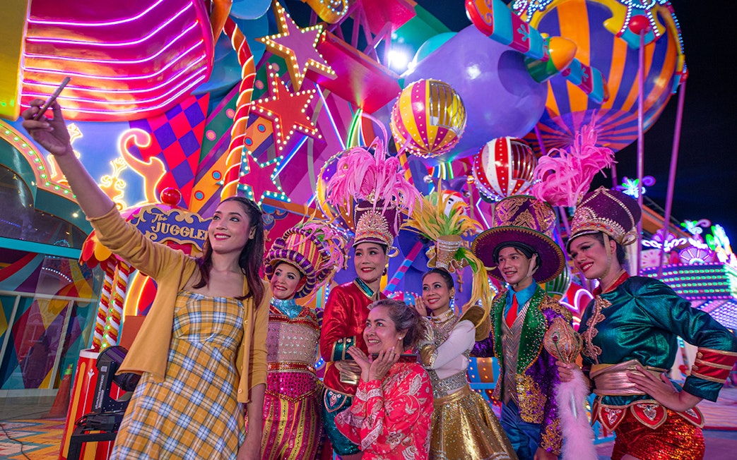 Carnival performers and visitors at Carnival Magic Park, vibrant costumes and lights.