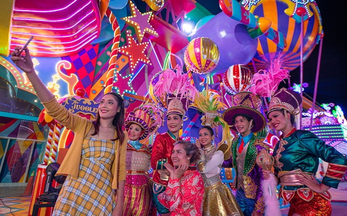 Carnival performers and visitors at Carnival Magic Park, vibrant costumes and lights.