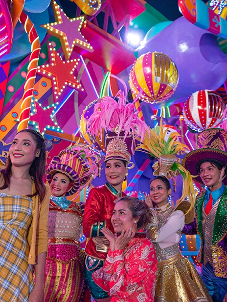 Carnival performers and visitors at Carnival Magic Park, vibrant costumes and lights.