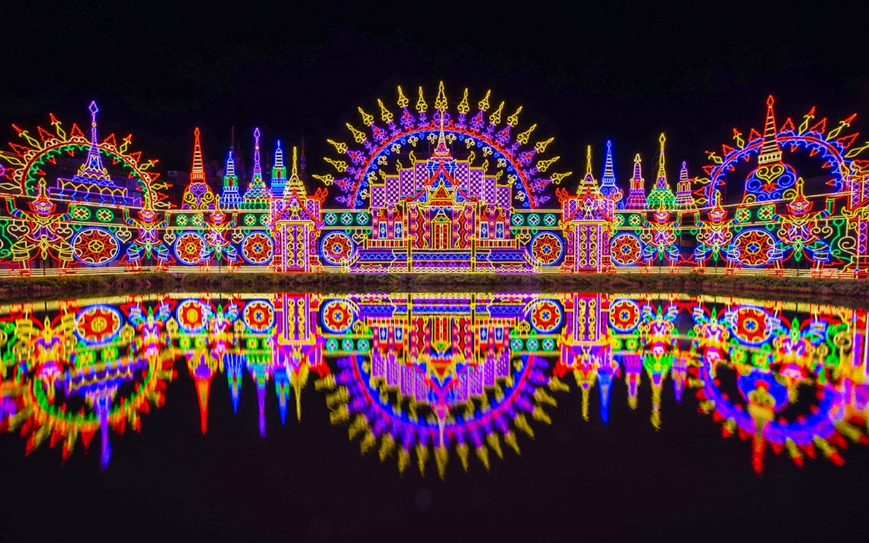 Colorful neon lights display at Carnival Magic Park, Phuket, reflecting in water.
