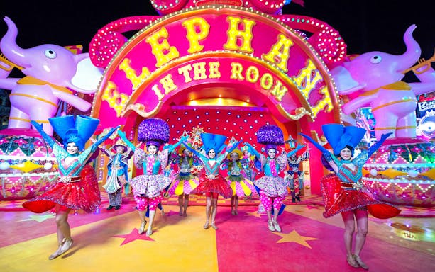 Performers in vibrant costumes at Carnival Magic Park, Phuket, under a colorful "Elephant in the Room" sign.