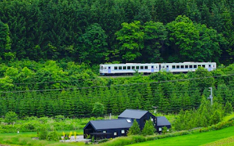 Train passing through lush forest in Shikoku, Japan, near a modern black house.