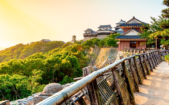 Matsuyama Castle on a hill with lush greenery, view from a wooden path, Shikoku, Japan.