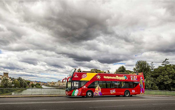 Florence hop-on hop-off bus near Arno River with cityscape in background.