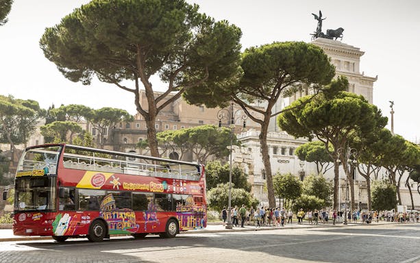 Open-top tour bus near Rome's Altare della Patria with tourists exploring.