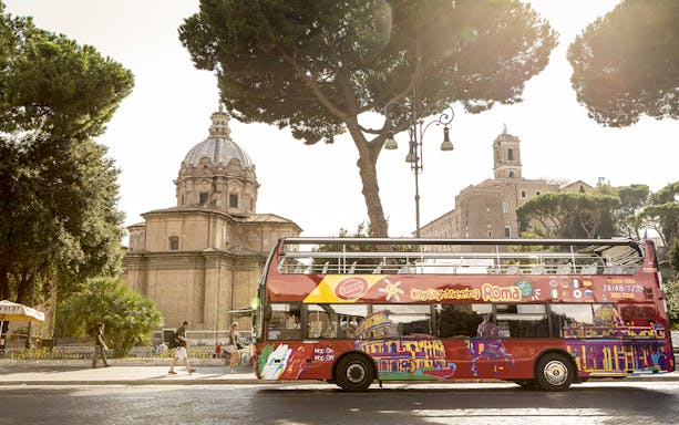 Open-top tour bus near Roman Forum in Rome, Italy, with historical buildings in the background.