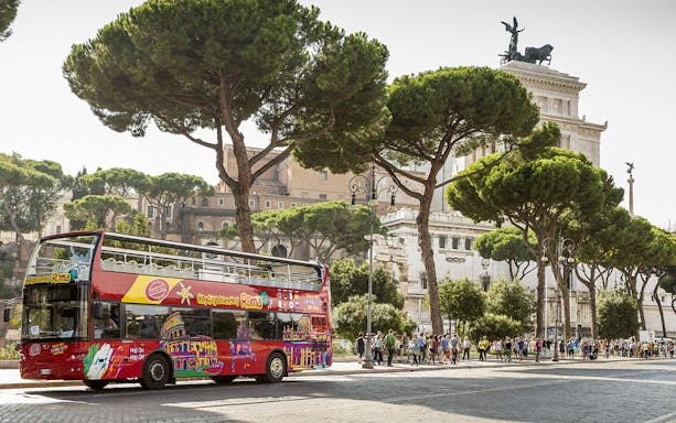 Open-top tour bus near St. Peter's Basilica in Rome with tourists and historic architecture.