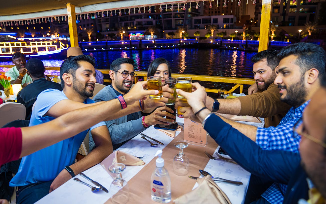 Guests toasting drinks on a Dhow Dinner Cruise on Dubai Creek at night.