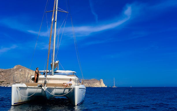 Catamaran sailing near rocky coastline during private sunset cruise with dinner.