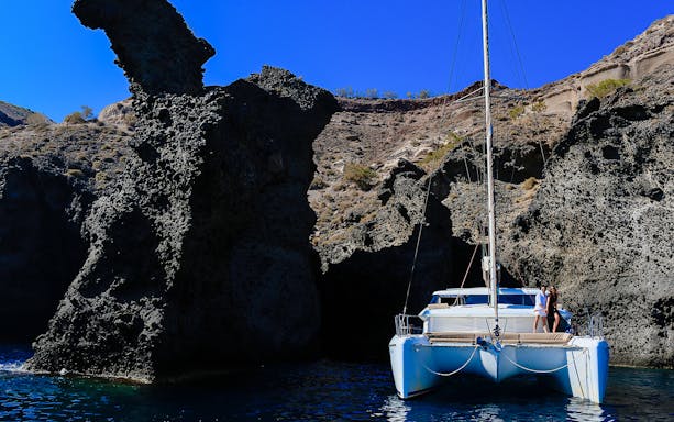 Catamaran sailing near rocky cliffs during a private sunset cruise with dinner.