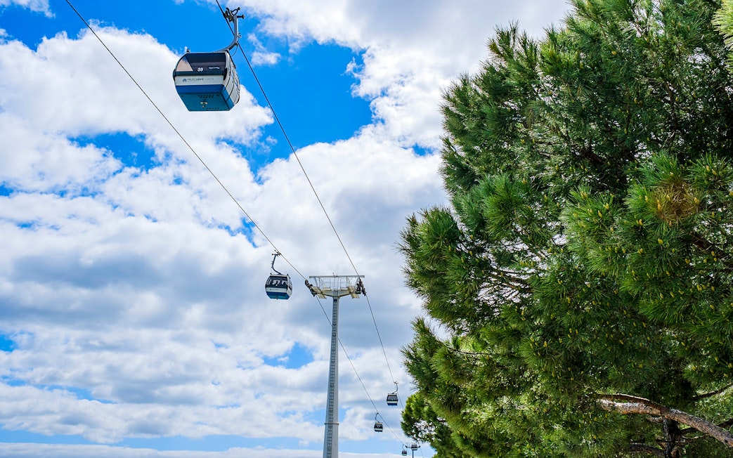 Telecabine cable cars in Lisbon, Portugal, gliding over trees and blue sky.