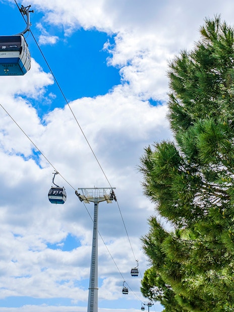Telecabine cable cars in Lisbon, Portugal, gliding over trees and blue sky.
