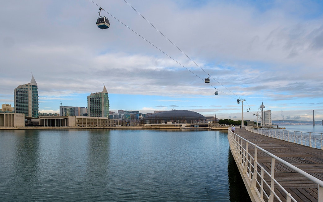 Telecabine cable cars over Tagus River in Lisbon, Portugal, with cityscape in the background.