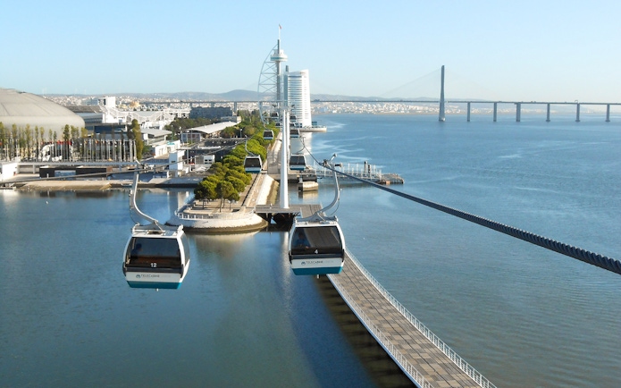 Telecabine cable cars over Tagus River in Lisbon with cityscape and bridge in view.