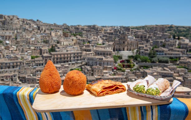 Traditional Sicilian dishes with Syracuse cityscape in the background.