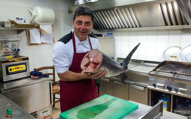 Chef holding a large fish in a Syracuse kitchen during a traditional cooking class.