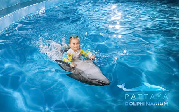 Child riding a dolphin at Pattaya Dolphinarium, Thailand.