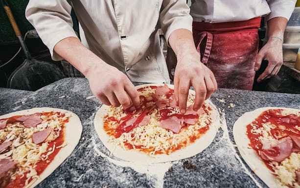 Hands preparing pizza with toppings during a Naples pizza making class.