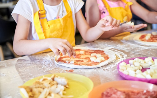 Children making pizza with cheese in a Naples cooking class.