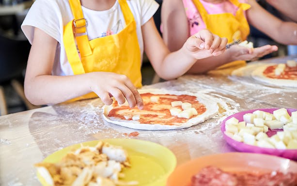 Children making pizza with cheese in a Naples cooking class.