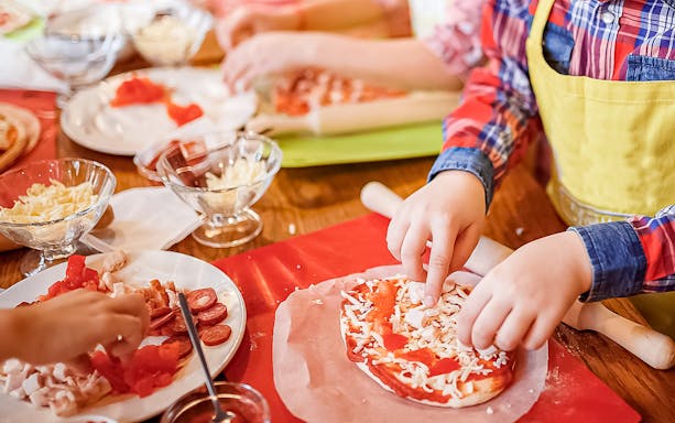 Children making pizza with toppings during a Naples pizza class.