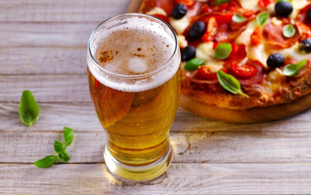 Glass of beer and pizza with olives and basil on a wooden table in Naples.