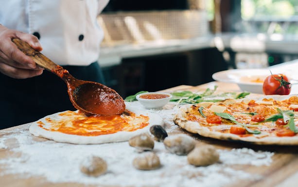 Pizza preparation with tomato sauce and fresh ingredients in Naples.