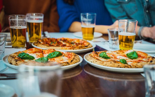 Three pizzas with basil and glasses of beer on a table during a food tasting in Naples.