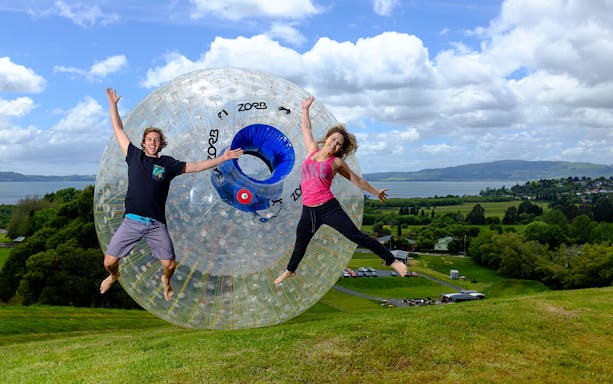 People enjoying Zorb Rotorua VIP Experience on a grassy hill with scenic lake view.