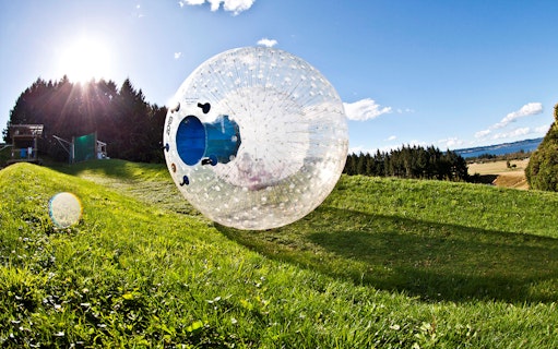Zorb rolling down a grassy hill in Rotorua, New Zealand, with scenic landscape in the background.