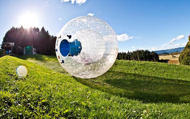 Zorb rolling down a grassy hill in Rotorua, New Zealand, with scenic landscape in the background.