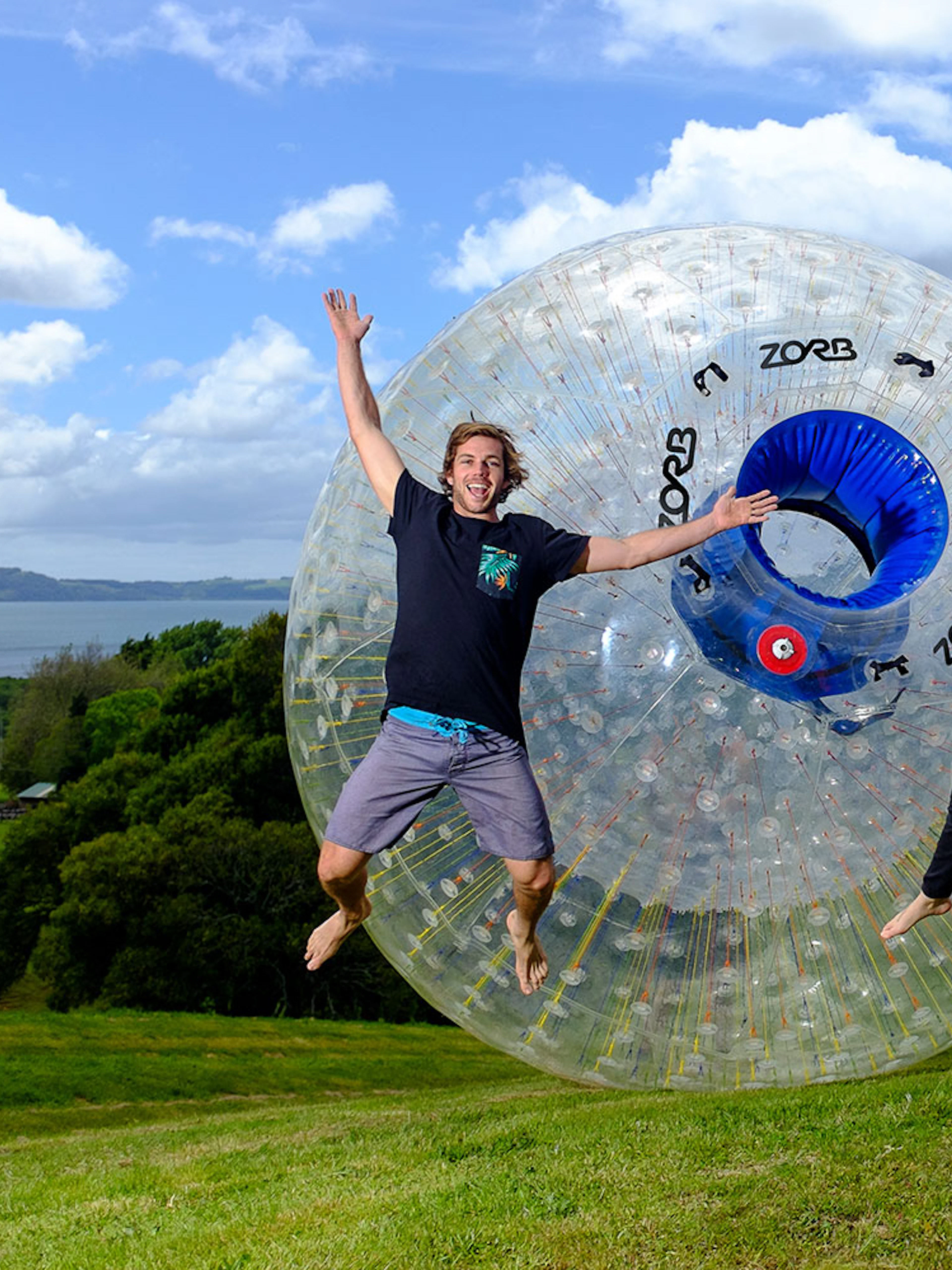 People enjoying ZORB Rotorua experience with scenic view of Lake Rotorua in the background.
