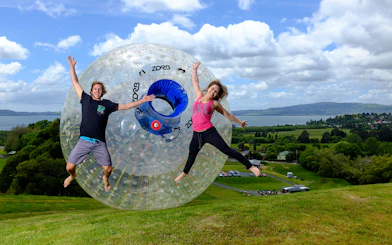People enjoying ZORB Rotorua experience with scenic view of Lake Rotorua in the background.