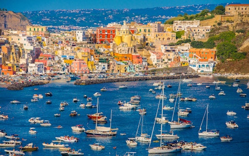 Boats in the harbor of colorful Procida Island, Italy, with vibrant buildings in the background.
