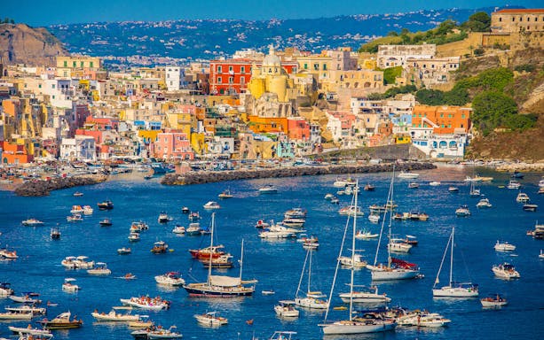 Boats in the harbor of colorful Procida Island, Italy, with vibrant buildings in the background.