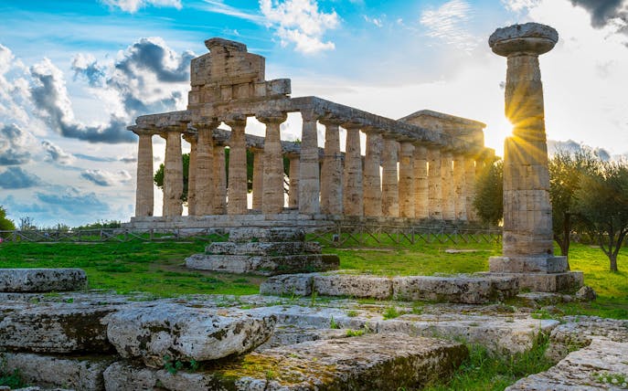 Ancient Greek temple ruins at Paestum, Italy, with sunlight streaming through columns.