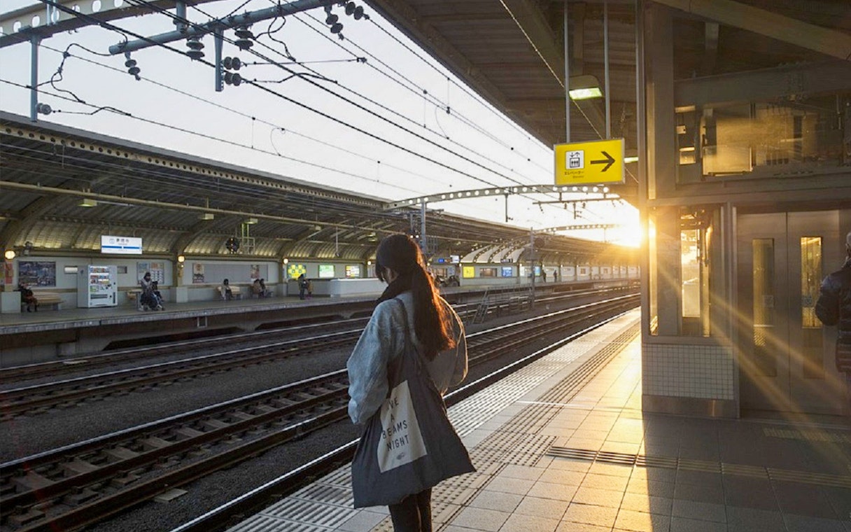 Person waiting at Tokyo train station platform during sunset.