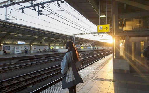 Person waiting at Tokyo train station platform during sunset.