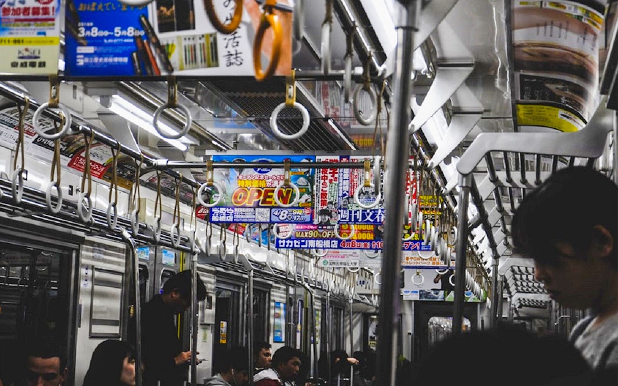 Tokyo subway interior with passengers and overhead advertisements.