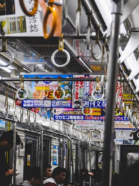 Tokyo subway interior with passengers and overhead advertisements.