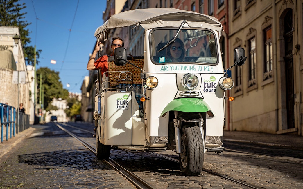 Tuk-tuk driving along Lisbon's 28 tram route with passengers enjoying the city view.