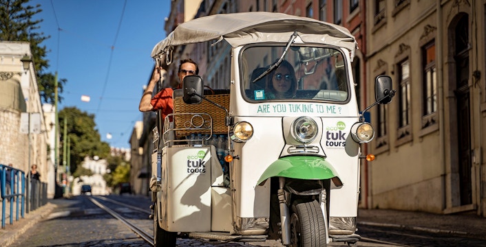 Tuk-tuk driving along Lisbon's 28 tram route with passengers enjoying the city view.