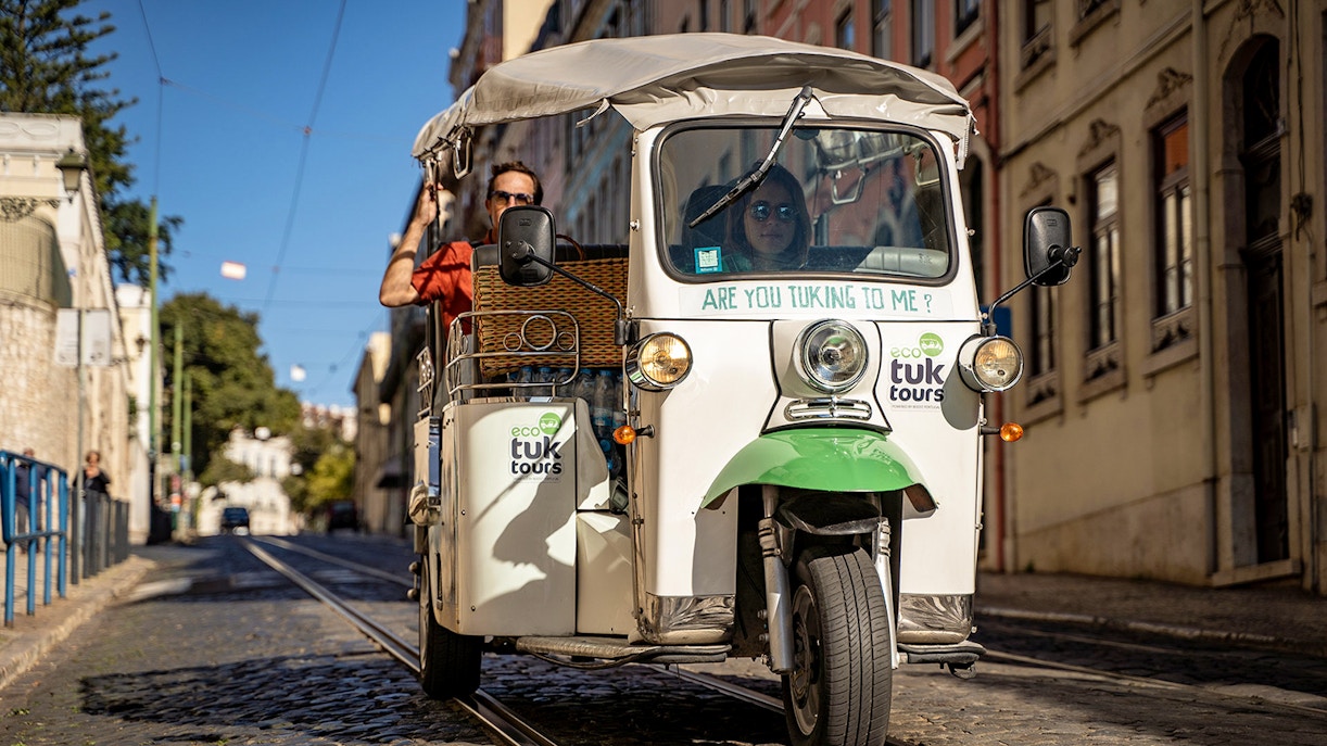Tuk-tuk driving along Lisbon's 28 tram route with passengers enjoying the city view.
