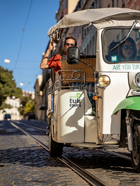Tuk-tuk driving along Lisbon's 28 tram route with passengers enjoying the city view.