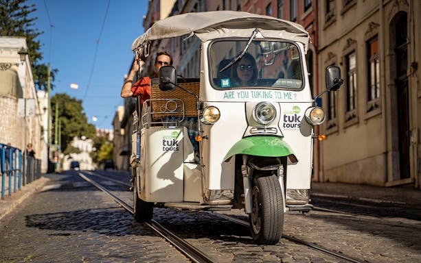 Tuk-tuk driving along Lisbon's 28 tram route with passengers enjoying the city view.